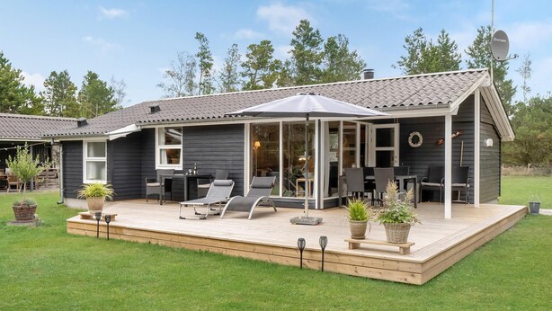 Ein modernes Haus mit überdachter Terrasse, Essbereich und großem Fenster mit Blick auf den Garten.