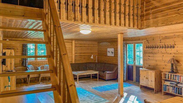 Een houten cabin met een slaaploft, een zithoek met een bank en een tafel, en een boekenkast.