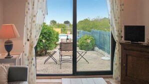 A room with a sofa, a TV on a wooden cabinet, a table with a bowl, and a view of an outdoor patio with a pool, chairs, and a blue fence. - Lovely home in Cadouarn with WiFi (Cadouarn)