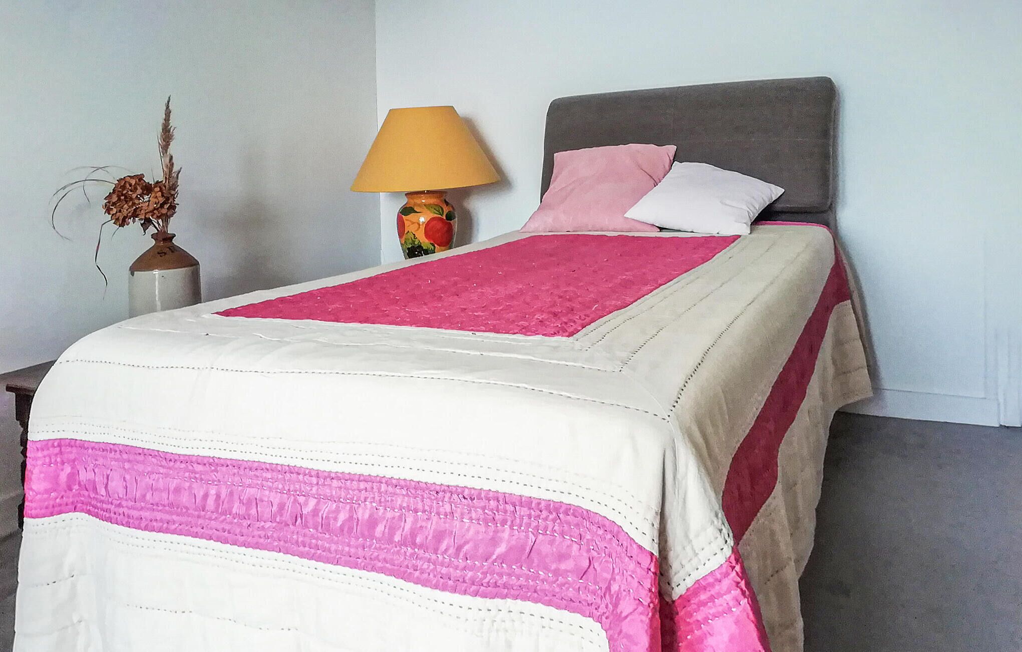 Un letto rifatto con una coperta bianco e rosa, una testiera grigia e due cuscini.