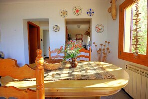 A dining area with a wooden table, a woven placemat, and a vase with flowers. There are decorative plates on the wall and a window with a view of greenery. - 44263 Romantic Sa Nau - 44263 Romantic vacation home Sa Nau (Colonia de Sant Pere)