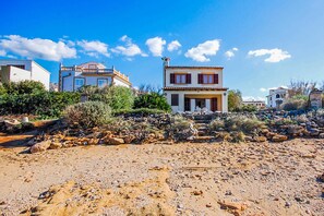 A coastal property with multiple buildings, a rocky foreground, and a clear blue sky.