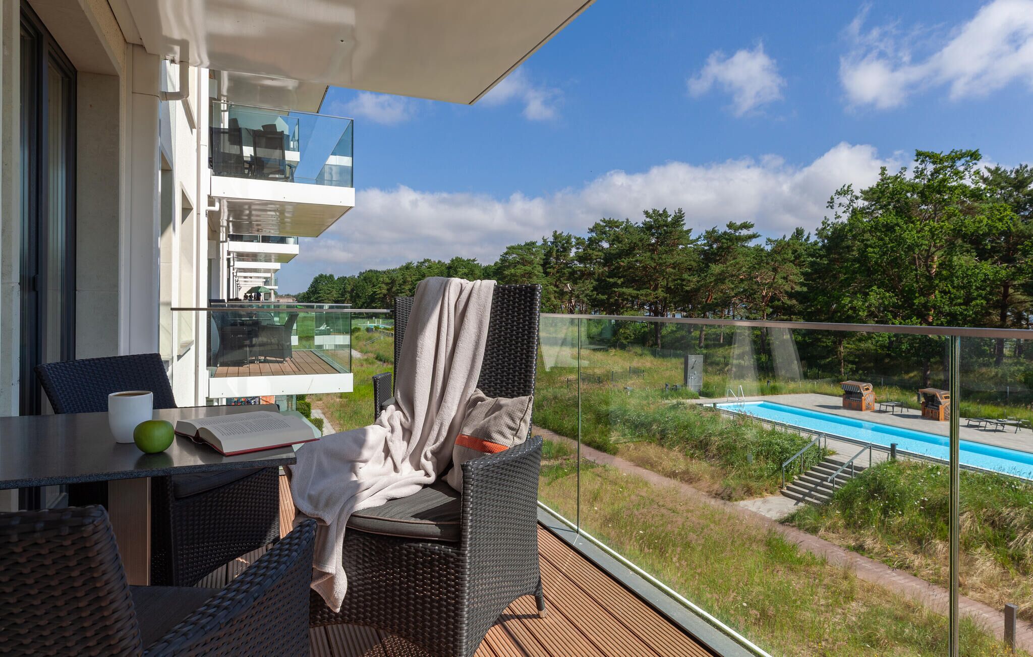 Een balkon met een tafel, stoelen en uitzicht op een zwembad.