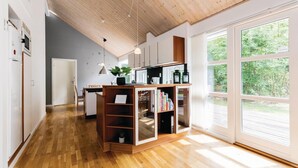 A modern kitchen with wooden cabinets, a built-in island with shelves, and large windows offering a view of greenery. - Nice home in Hasle with sauna (Hasle)