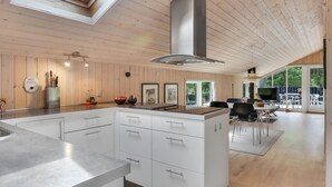 Een moderne keuken met een centraal eiland, houten lambrisering en een groot raam met uitzicht op groen.