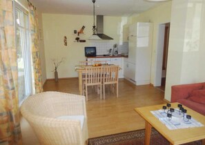 A living room with a sofa, a dining table with chairs, a kitchen area with a stove, and a refrigerator.