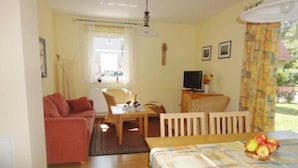 A room with a sofa, a dining table with chairs, a television, and a window with curtains.