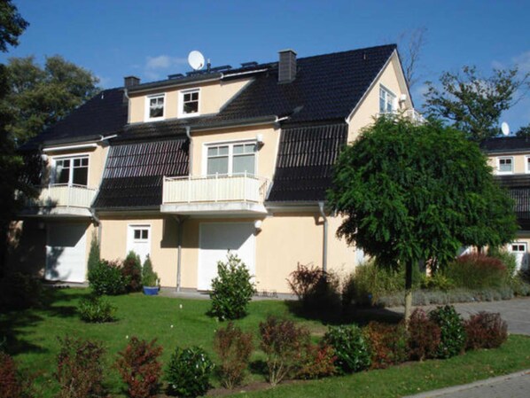 A two-story residential building with a balcony, satellite dish, and a well-maintained lawn.