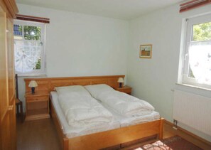 A bedroom with a wooden bed, two bedside tables with lamps, a window with blinds, and a radiator.