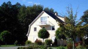 A two-story house with a balcony, surrounded by trees and a well-maintained garden.