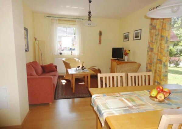 A room with a sofa, a dining table with chairs, a television, and a window with curtains.