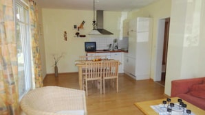 A living room with a sofa, a dining table with chairs, a kitchen area with a stove, and a refrigerator.