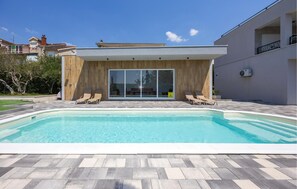 A modern pool area with a clear pool, two lounge chairs, and a wooden deck. - Cozy apartment in Kastel Stafilic (Kastel Stafilic)
