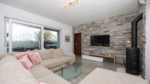 Ein modernes Wohnzimmer mit Steinwand, Flachbildfernseher, Glastisch und einer Couch mit rosafarbenen Kissen.