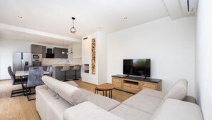 Ein modernes Wohnzimmer mit einer Couch, einem Fernseher und einer Küchenzeile im Hintergrund.