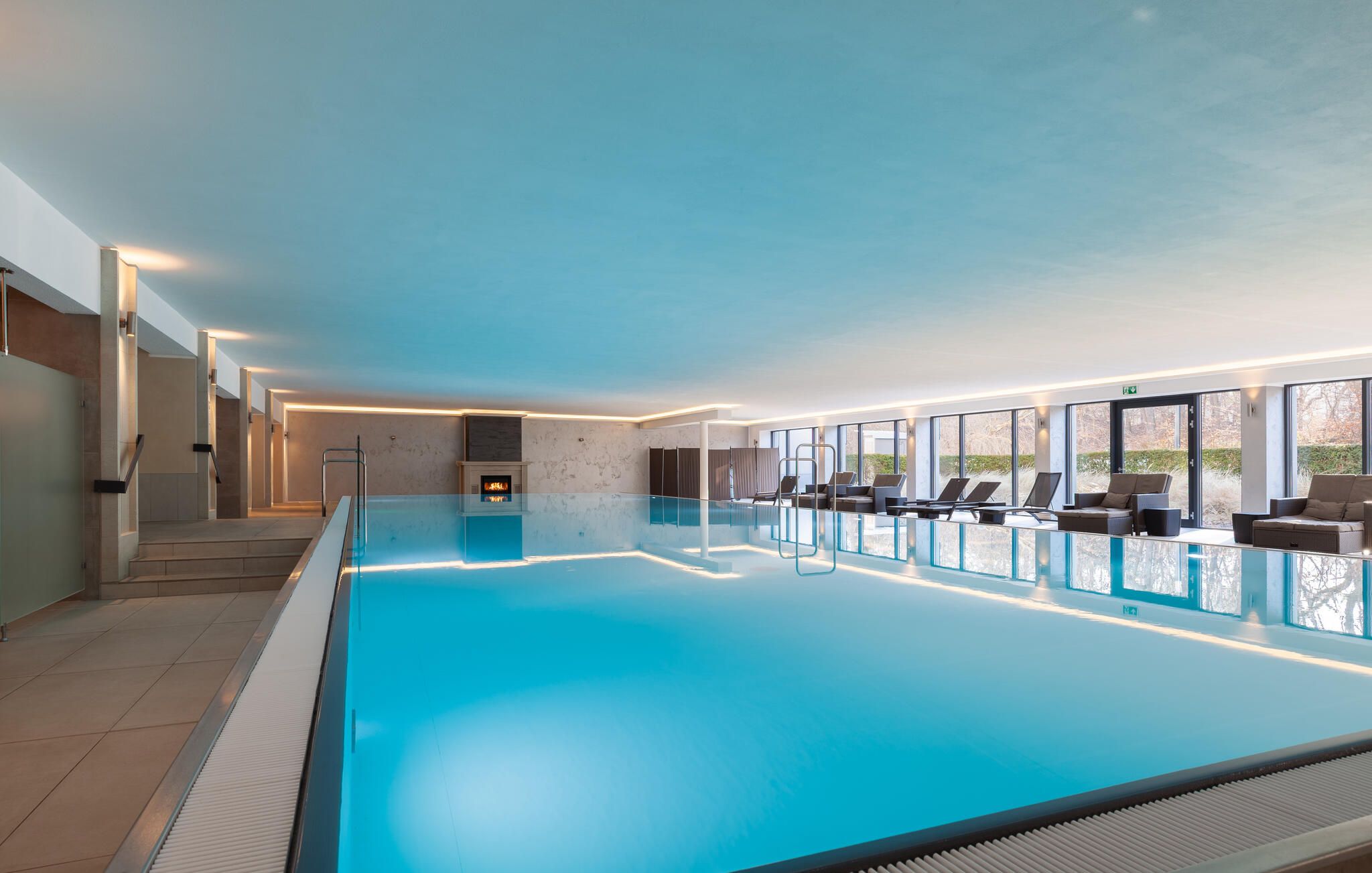 A large indoor swimming pool with a fireplace, sun loungers, and a view of the outdoors.