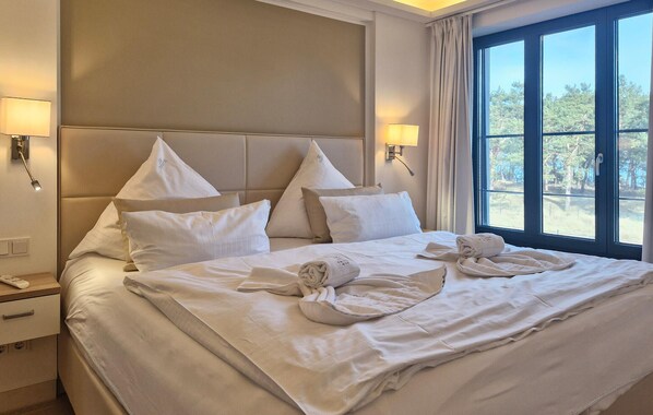 A hotel room with a large bed, two bedside lamps, a nightstand, and a window with a view of trees.