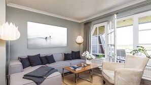 Un salon moderne avec un canapé gris, une table basse en bois et un fauteuil beige. Une grande fenêtre offre une vue sur l’extérieur.