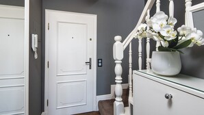 Un couloir avec une porte blanche, un escalier avec des balustrades blanches et un vase rempli de fleurs blanches, posé sur une vitrine en verre.