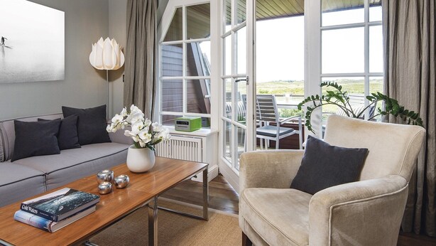 Un salon moderne comprenant un canapé, un fauteuil, une table basse et offrant une vue sur l’extérieur grâce à de grandes fenêtres.
