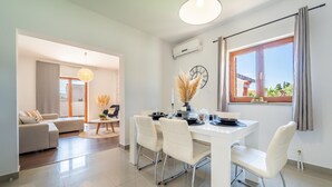 A modern living room with a sofa, a dining table set for four, and a large window with curtains. - Gorgeous home in Biograd (Biograd)