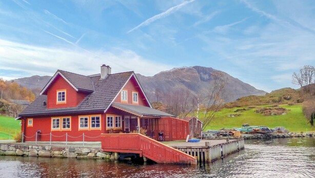 Et rødt hus med en dok, der strækker sig ud i en sø, omgivet af bjerge og grønt.