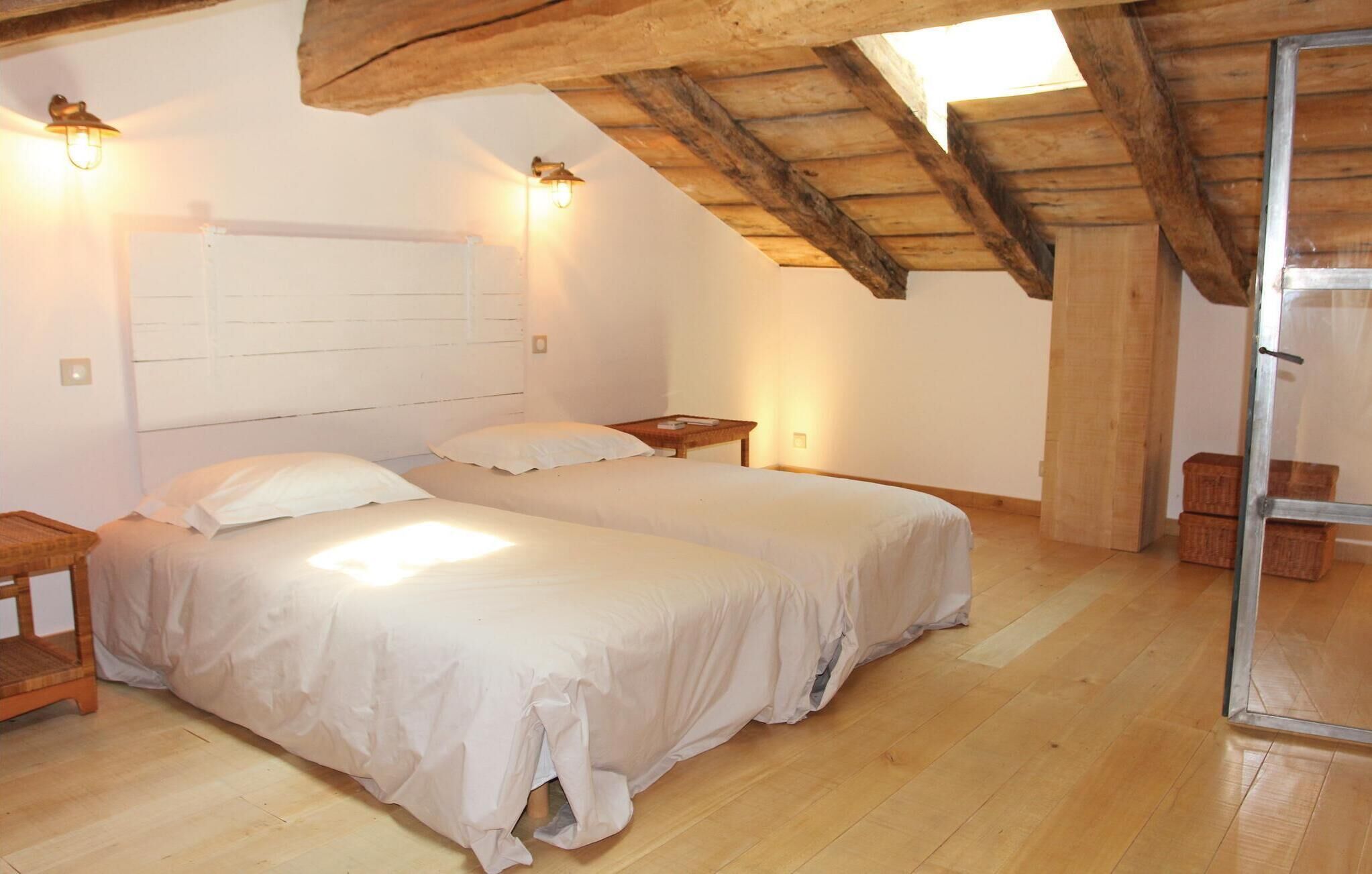 Quarto com duas camas, pisos de madeira, teto inclinado e uma pequena mesa com abajur.