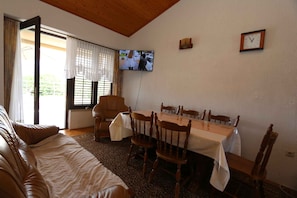 Una habitación con cama, una mesa de comedor con sillas, un televisor montado en la pared y una ventana con cortinas.