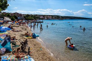 Enjoy a family-friendly beach experience with umbrellas, chairs, and a stroller, surrounded by swimmers and sunbathers.