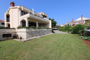 Stunning two-story building with a flat roof and balcony, set amidst a beautifully manicured lawn and lush greenery.