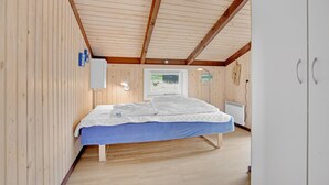 Un dormitorio con techo de madera, una cama con cubrecama azul, un radiador blanco y una ventana con vista a zonas verdes.