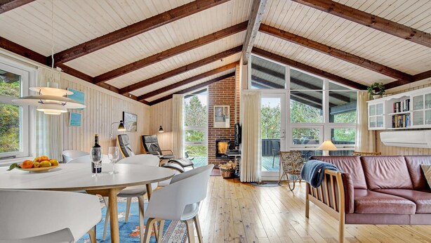 Amplia sala de estar con techo alto, vigas de madera, chimenea y un gran ventanal con vistas al exterior.