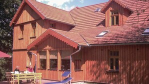 A wooden house with a sloped roof, multiple windows, and a patio area with a table and chairs. - 2 bedroom cozy home in Dautphetal (Dautphetal)