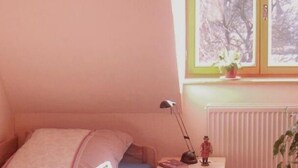 A bedroom with a wooden bed, a nightstand with a lamp, a window with a view of trees, and a radiator. - 2 bedroom cozy home in Dautphetal (Dautphetal)