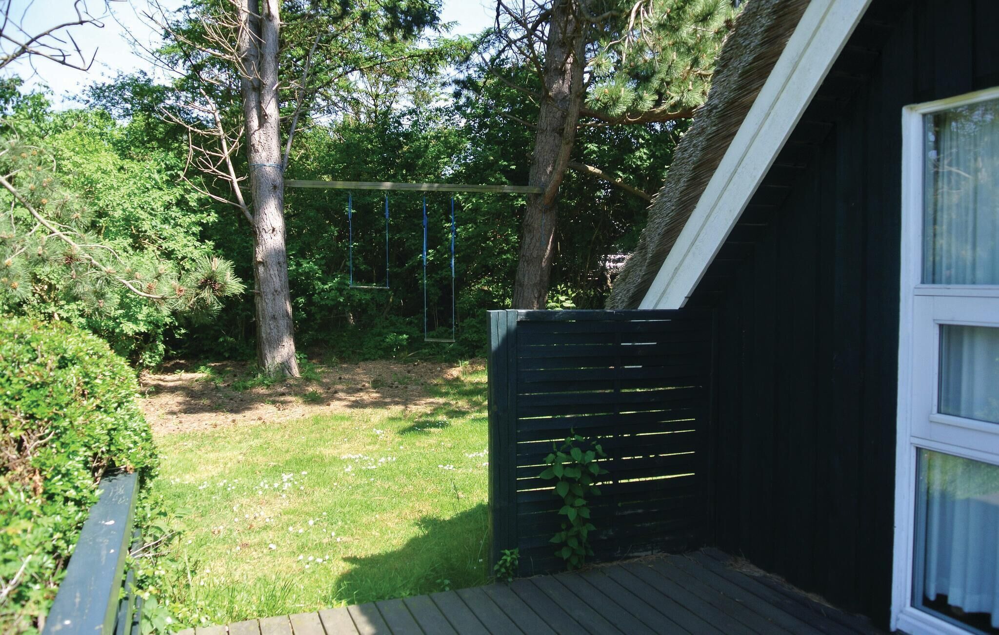 Een houten terras dat leidt naar een zwart gebouw met een raam.