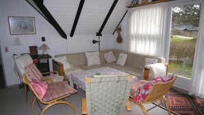 A cozy room with a checkered sofa, two wicker chairs, a small table, and a view of the outdoors through a window.