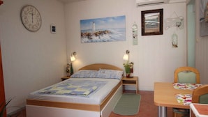 A bedroom with a bed, bedside tables, a painting of a lighthouse, a clock, and a small table with chairs. - Studio with balcony and air conditioning (Šilo)