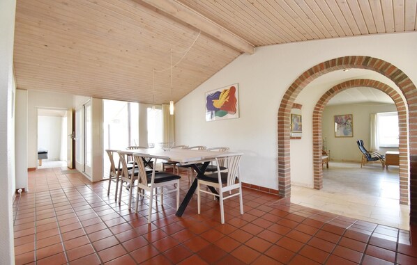 Una stanza spaziosa con pavimento piastrellato, soffitto in legno e un'area da pranzo con tavolo e sedie.