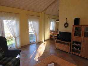 A living room with a sofa, TV, wooden cabinet, and a dining area with chairs and a table.