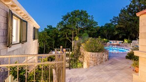 Un sendero de piedra conduce a una zona de piscina con un muro de piedra y abundante vegetación.