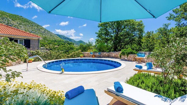 Un área de piscina con muro de piedra, sillones de descanso y una sombrilla grande.