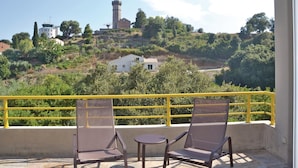 A balcony with two chairs and a small table, overlooking a hill with a lighthouse and buildings. - Cozy home in San Giuliano with WiFi (San Giuliano)