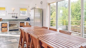 A modern kitchen with a large dining table and chairs, a refrigerator, and a view of greenery through large windows. - Cozy home in San Giuliano with WiFi (San Giuliano)