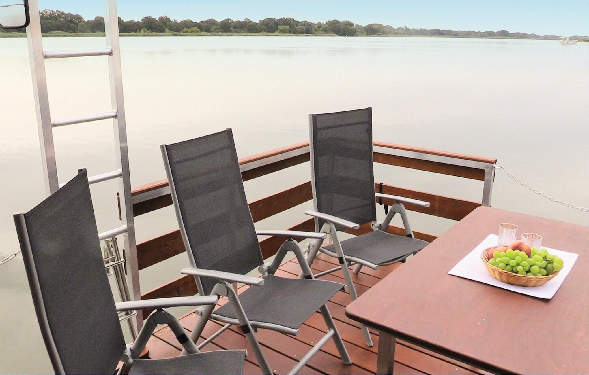 Eine Terrasse mit vier Stühlen und einem Tisch, mit Blick auf ruhiges Wasser.