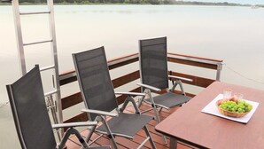 Une terrasse avec quatre chaises et une table, donnant sur une étendue d’eau calme.