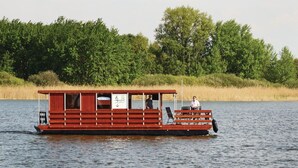 Un pédalo rouge doté d’une zone de sièges abritée et d’un petit pont, flottant sur une eau calme.