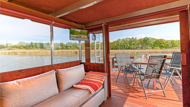 Une terrasse avec un canapé et des fauteuils, donnant sur une étendue d’eau et des arbres.
