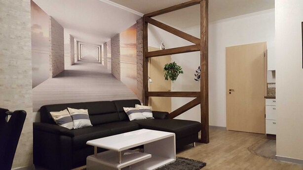 Un salon moderne avec un canapé noir, une table basse blanche et un mur d’accent en bois.