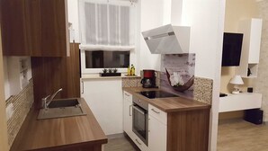 Une cuisine compacte équipée d’un évier, d’une cuisinière et d’un petit plan de travail. Une fenêtre est agrémentée d’un rideau léger et un appareil à café est posé sur le plan de travail.