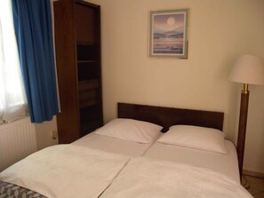 Une chambre à coucher avec un lit, une table de chevet, une lampe, une fenêtre avec des rideaux et un tableau au mur.